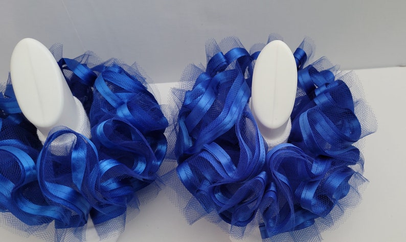 Pu&ograve; includere: Due fiocchi per capelli in tulle e raso blu su supporti di esposizione bianchi. I fiocchi sono realizzati in tulle blu e nastro di raso.