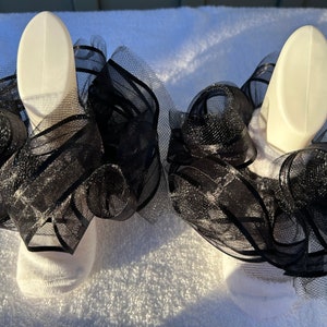 May include: A pair of white socks with black tulle ruffles around the ankles. The ruffles are layered and have a sparkly finish.