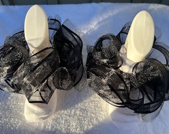 May include: A pair of white socks with black tulle ruffles around the ankles. The ruffles are layered and have a sparkly finish.