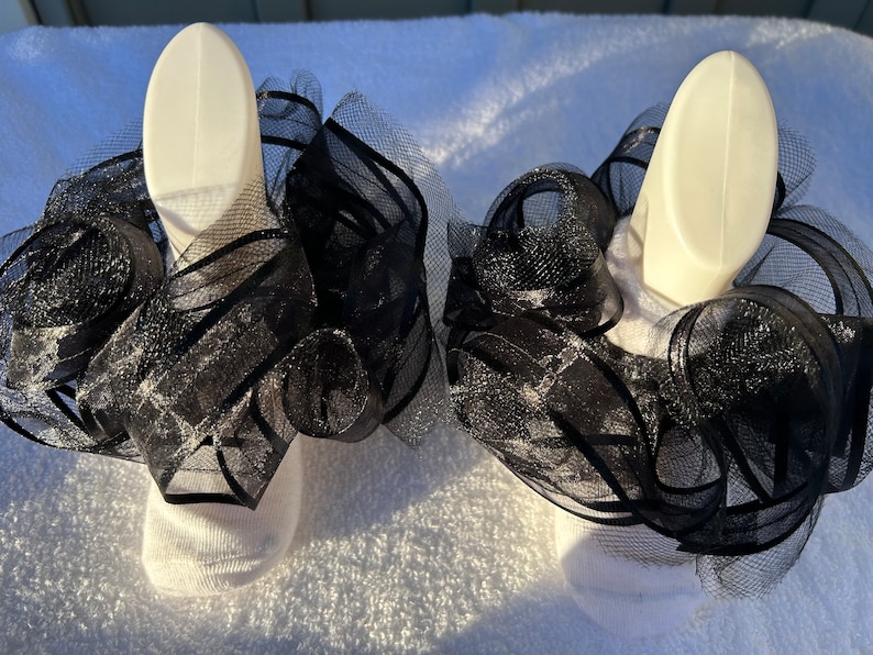 May include: A pair of white socks with black tulle ruffles around the ankles. The ruffles are layered and have a sparkly finish.