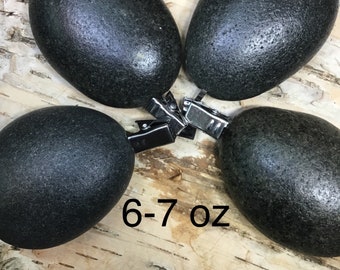 May include: Four smooth, black, oval-shaped stones, each weighing 6-7 ounces, are arranged in a star pattern on a light brown, textured surface.