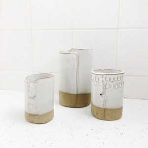 May include: Three white ceramic vases with brown accents. The vases are of different sizes and have a rustic, handmade look.