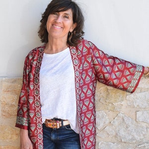 May include: A woman wearing a red and white patterned kimono with a white t-shirt and blue jeans.