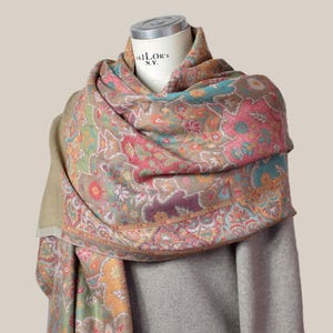 Peut inclure: Écharpe à motifs cachemire avec un motif floral aux accents roses, turquoise, orange et violets sur fond beige. L'écharpe est drapée sur un mannequin. Le mannequin porte l'inscription "TAILOR'S N.Y.".