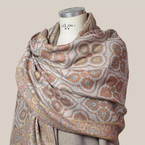 Peut inclure: Un châle à motifs drapé sur un mannequin. Le châle présente un motif répétitif dans des tons d'orange, de bleu et de rose sur un fond gris clair. La bordure présente un motif floral détaillé avec des accents dorés. Le mannequin porte l'inscription "TAILOR'S N.Y.".