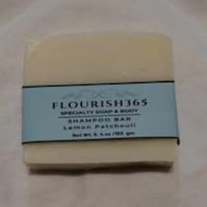 May include: A white bar of shampoo soap with a blue label that reads "FLOURISH365 SPECIALTY SOAP & BODY SHAMPOO BAR Lemon Patchouli Net Wt. 5 oz/142 gm"