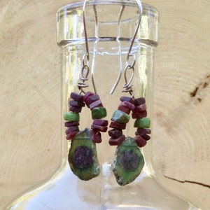 May include: A pair of silver earrings with green and red gemstone beads. The earrings feature a large, green and red gemstone pendant.