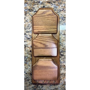 May include: A wooden mail organizer with three compartments and four key hooks. The organizer is made of light brown wood with a visible wood grain pattern. The compartments are shaped with a decorative top edge.