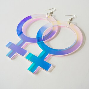 May include: A pair of iridescent blue and pink acrylic earrings shaped like the female gender symbol.