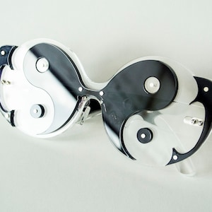 May include: Clear plastic sunglasses with a yin yang design in black and white. The lenses are mirrored and the frames are shaped like a butterfly.