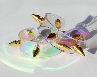 May include: Three iridescent clear plastic bracelets with gold spikes. The bracelets are stacked on top of each other.