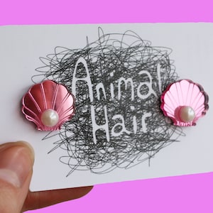 Könnte beinhalten: Zwei rosa Muschel-Haarklammern mit Perlenakzent. Die Klammern befinden sich auf einer weißen Karte mit dem Text "Animal Hair" in Schwarz.