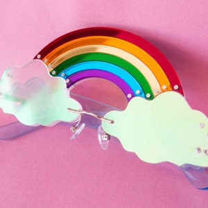 May include: Rainbow-coloured glasses with cloud-shaped frames. The rainbow is made of red, orange, yellow, green, blue, indigo, and violet. The clouds are a light green colour.