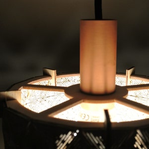 May include: A wooden pendant light with a geometric pattern and a copper finish. The light is hanging from a black cord and has a copper ceiling mount. The light is on and illuminating the pattern.