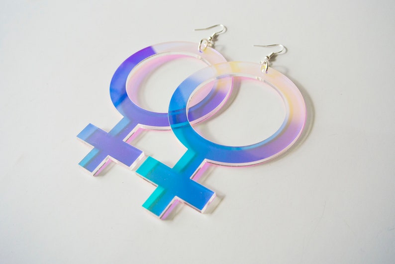 May include: A pair of iridescent blue and pink acrylic earrings shaped like the female gender symbol.