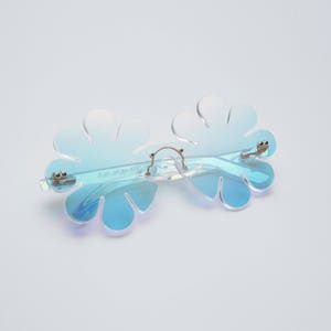 May include: Blue iridescent flower-shaped sunglasses with a silver metal frame.