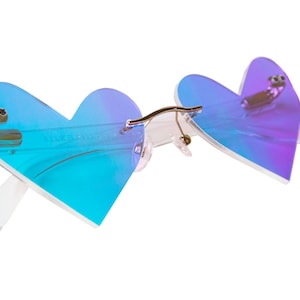 May include: Heart-shaped sunglasses with a blue and purple iridescent lens. The frame is white and the arms are clear.