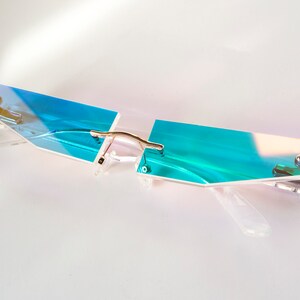Puede incluir: Un par de gafas con montura transparente azul iridiscente y puente de metal plateado.
