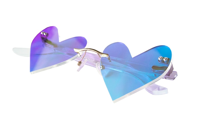 May include: Heart-shaped sunglasses with a iridescent blue and purple gradient lens. The frame is clear plastic with gold accents.