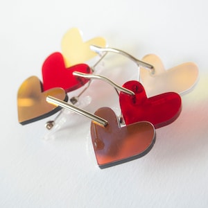 Puede incluir: Un par de gafas de sol con forma de corazón con montura plateada. Las lentes están superpuestas en diferentes colores: marrón, rojo y amarillo.