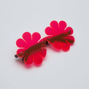 May include: A pair of pink flower-shaped sunglasses with a black frame.