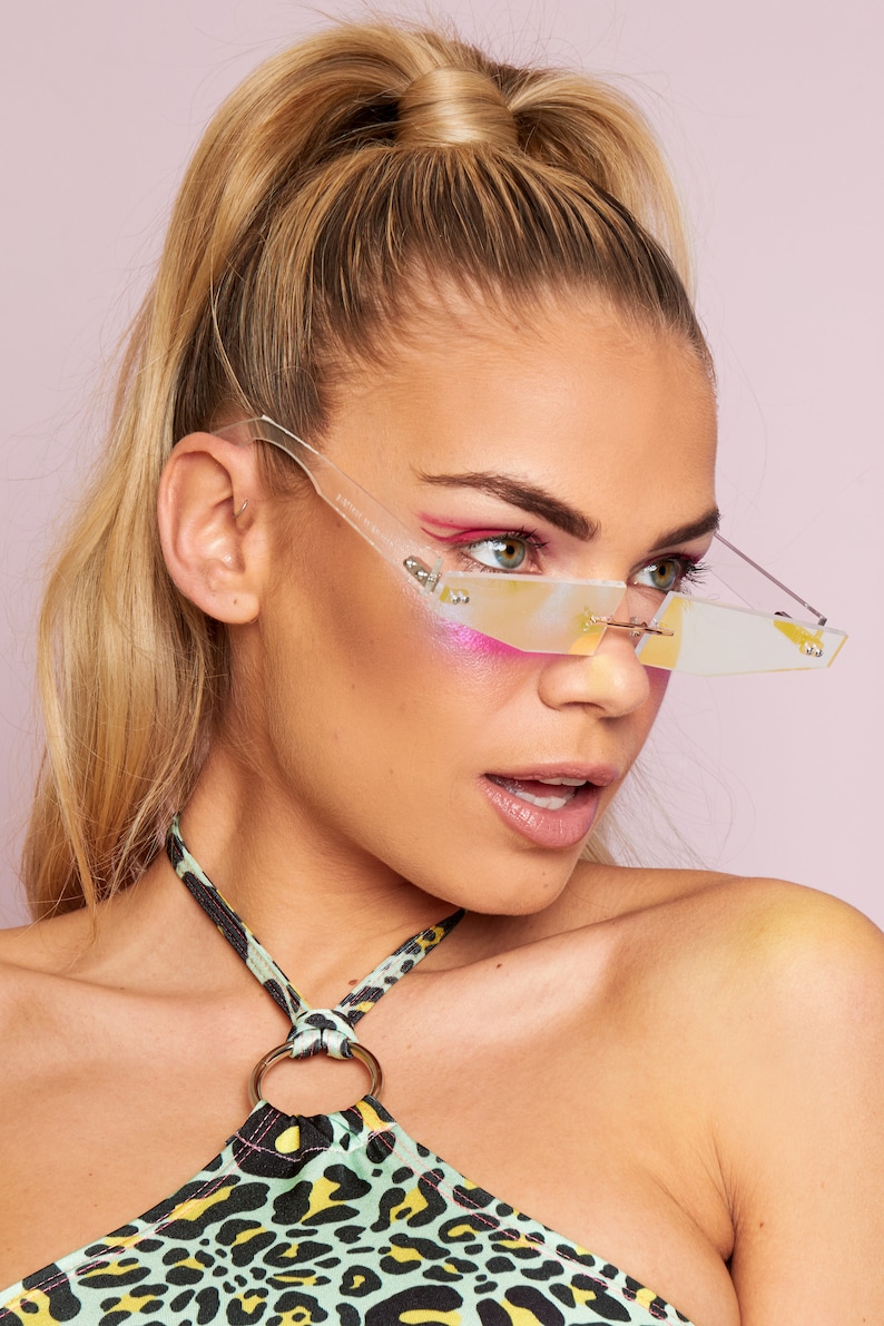 Puede incluir: Una mujer lleva un top halter de estampado de leopardo verde y negro con un anillo dorado. Lleva gafas de sol transparentes e iridiscentes con un marco fino.