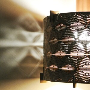 May include: A geometric patterned lampshade made of wood with a light shining through the intricate design.
