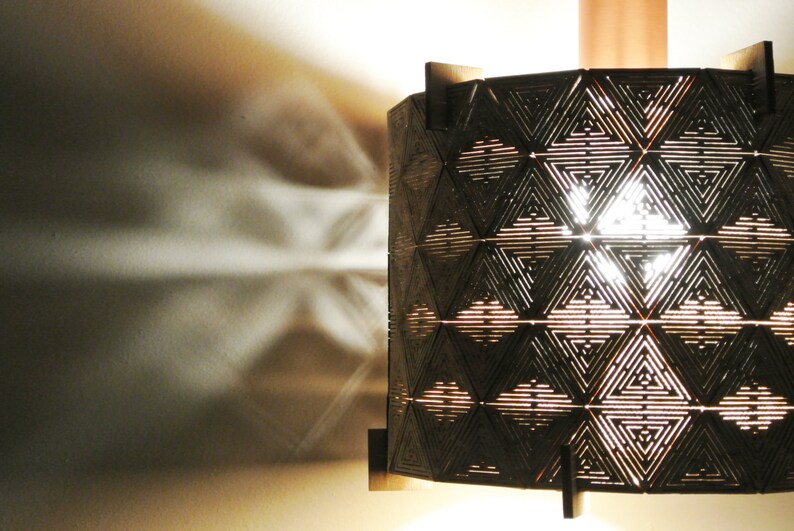 May include: A geometric patterned lampshade made of wood with a light shining through the intricate design.