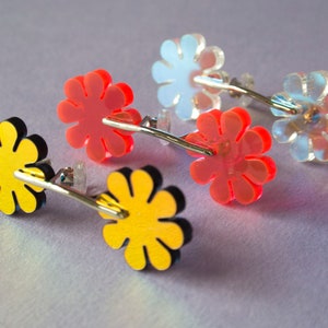 Puede incluir: Pendientes de botón con forma de flor en amarillo, rojo e iridiscente. Los pendientes tienen postes plateados y se presentan sobre un fondo morado claro. El diseño floral es encantador.
