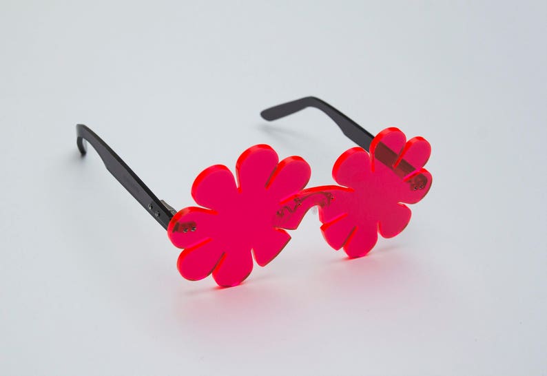 May include: Pink flower-shaped sunglasses with black arms. The sunglasses have a unique design with multiple petals.