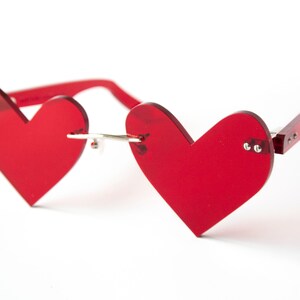 May include: Red heart-shaped sunglasses with a silver bridge and red plastic arms.