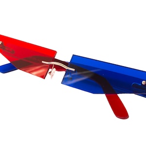 Puede incluir: Gafas de sol tintadas de rojo y azul con un dise&ntilde;o angular &uacute;nico. Las gafas tienen un puente y patillas de metal plateado.