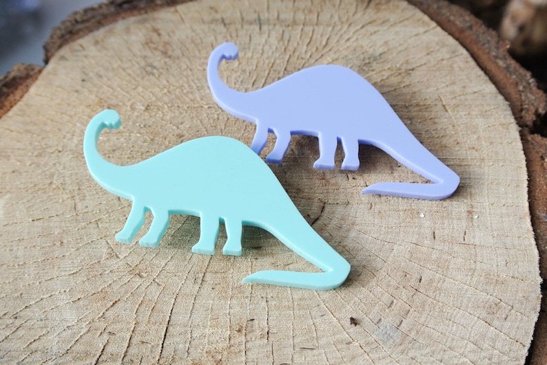 Pode incluir: Duas formas de dinossauro de pl&aacute;stico, uma azul claro e outra lavanda, sobre uma superf&iacute;cie de madeira.