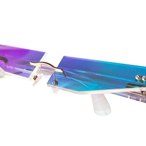 May include: A pair of rimless glasses with a blue and purple gradient lens. The glasses have a unique, angular design and are made of clear plastic.