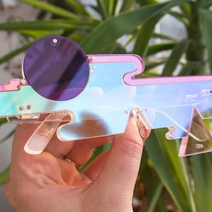 May include: A pair of iridescent pink and blue sunglasses with a round, purple lens. The sunglasses are made of plastic and have a unique, geometric design.