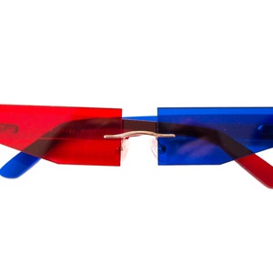 Puede incluir: Gafas de sol de pl&aacute;stico rojo y azul con un puente de metal delgado. Las gafas tienen una forma geom&eacute;trica con bordes angulados.