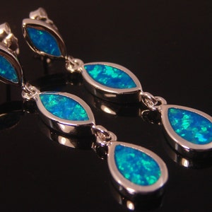 May include: A pair of silver dangle earrings with three teardrop-shaped blue opal stones.