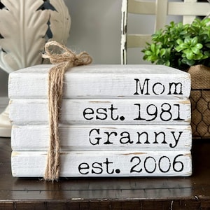 May include: A stack of four white books with black text. The top book says "Mom est. 1981", the second book says "Granny est. 2006".