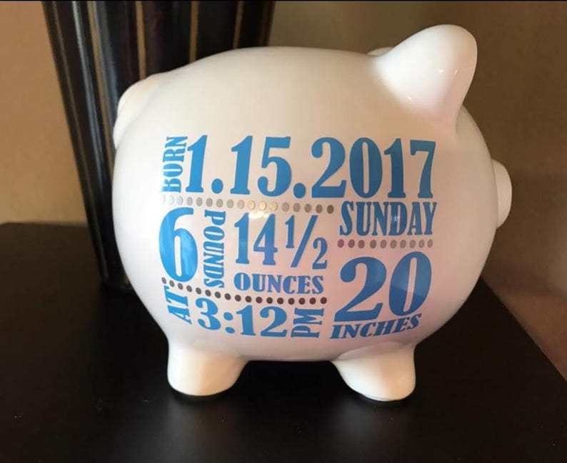 Peut inclure: Tirelire en c&eacute;ramique blanche avec texte bleu. Le texte comprend la date 1.15.2017, le poids 2,7 kg, la longueur 50,8 cm et l'heure 15h12. La tirelire a quatre petits pieds et une fente sur le dessus pour ins&eacute;rer des pi&egrave;ces.