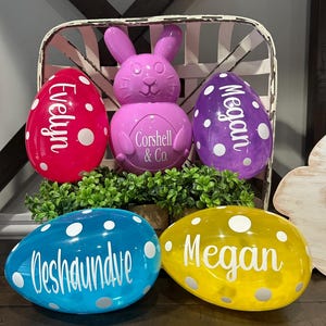 May include: An Easter-themed display featuring a purple bunny and four large, egg-shaped decorations. The eggs are in red, purple, blue, and yellow, each with white polka dots and a name. The bunny has the text "Corshell & Co."