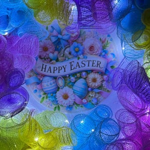 May include: A colorful Easter wreath made of mesh with a Happy Easter sign in the center. The wreath is decorated with lights and has a rainbow of colors, including purple, blue, green, and yellow.