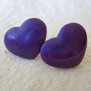 Puede incluir: Dos pendientes de color morado en forma de coraz&oacute;n con una superficie texturizada.