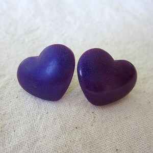 Puede incluir: Un par de pendientes de color morado en forma de coraz&oacute;n. Los pendientes tienen una textura moteada.
