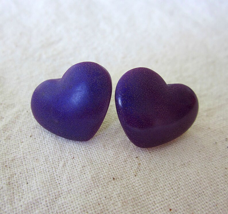 Puede incluir: Un par de pendientes de color morado en forma de coraz&oacute;n. Los pendientes tienen una textura moteada.