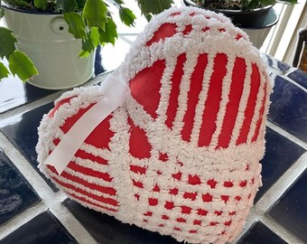 May include: A red and white heart-shaped pillow with a white bow. The pillow is made of a soft, fluffy material and has a textured surface.