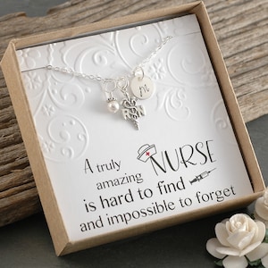 May include: A silver necklace with a charm that says "RN" and a small pearl charm. The necklace is in a box with a white card that says "A truly amazing nurse is hard to find and impossible to forget".