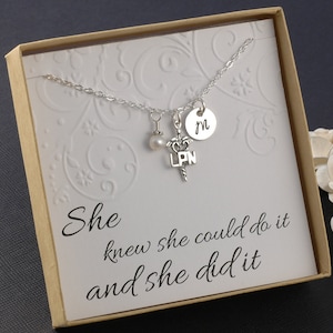 May include: A silver necklace with a pearl charm, a medical symbol charm with the letters "LPN" and a silver disc charm with the letter "M". The necklace is in a box with the text "She knew she could do it and she did it".
