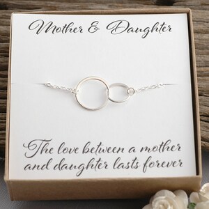 May include: A silver bracelet with two interlocking circles, presented in a gift box with the text "Mother & Daughter" and "The love between a mother and daughter lasts forever".
