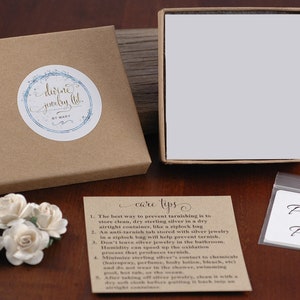 May include: A brown box with a white label that says "dirne jewelry ltd. by mary" and a white box with a white lid. There is a small white card with the text "care tips" and a list of instructions for caring for sterling silver jewelry. There is also a small white bag with the text "Polish Pad".