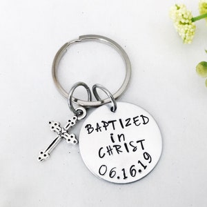 Puede incluir: Llavero de plata con un pequeño dije de cruz y una etiqueta redonda que dice "Bautizado en Cristo 06.16.19".